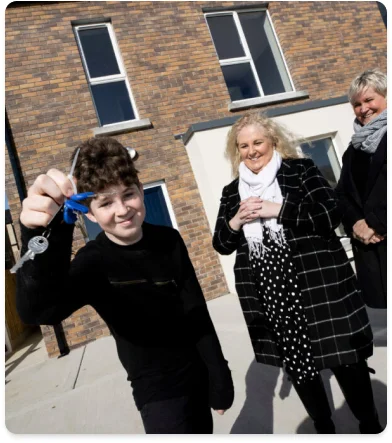 a child holding a key and smiling with a person and a brick building
