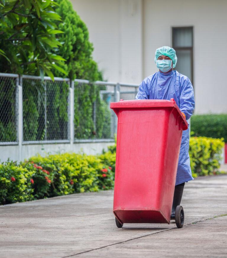 Hospital worker wheeling a red wheelie bin